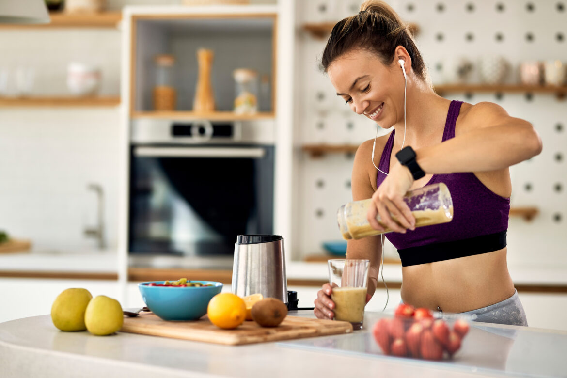 Happy sportswoman pouring fruit smoothie in a glass in the kitchen.